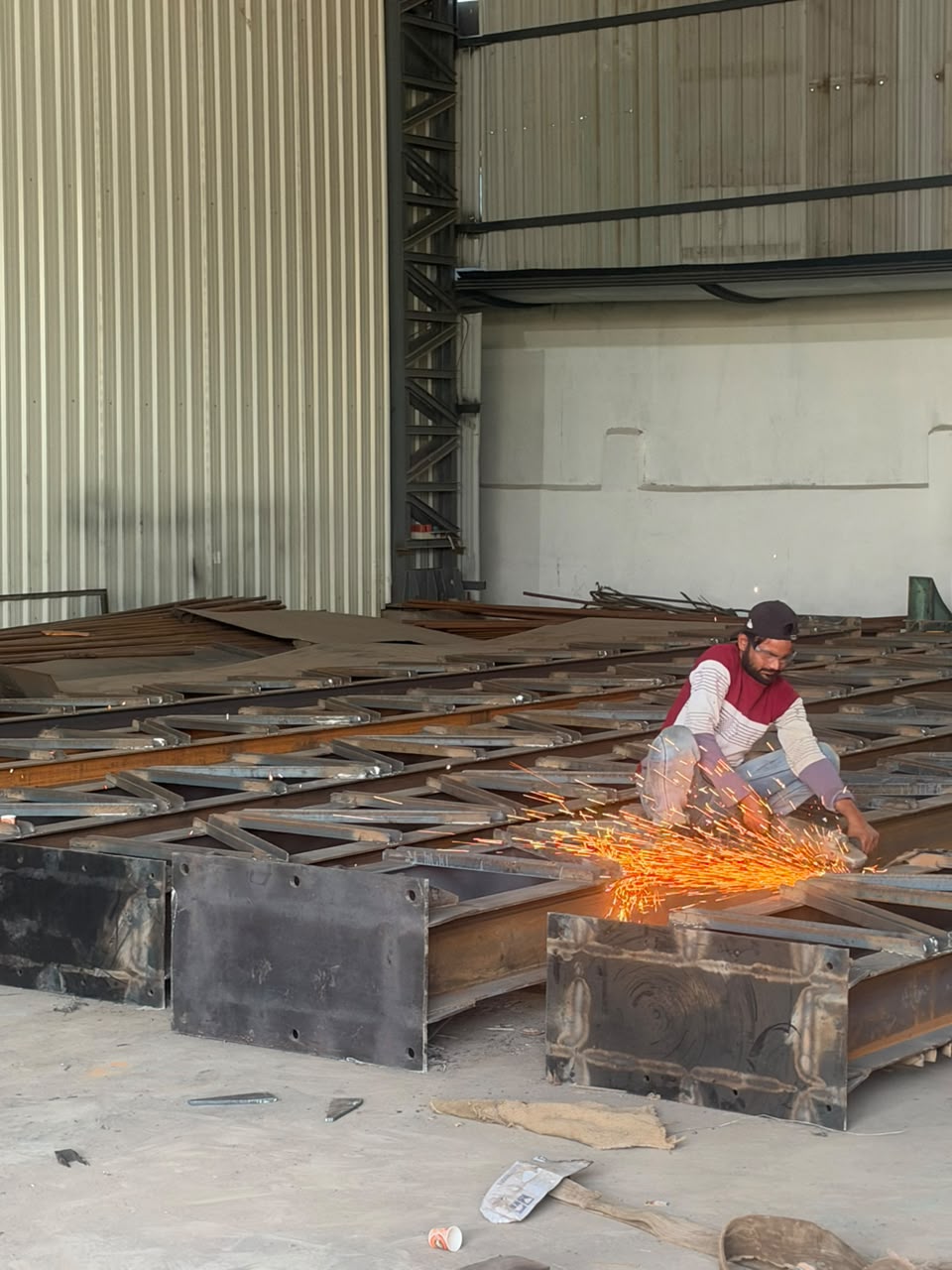 Industrial welder grinding structural I-beam flange joint inside SKEM fabrication shed